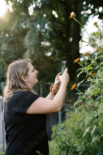 smiling gardener taking phone picture of tithonia mexican sunflower photo