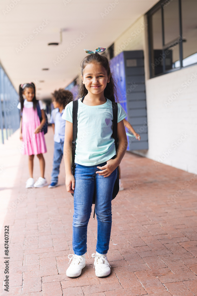 Biracial girl with backpack standing outside school, smiling confidently