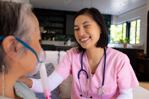 Asian nurse wearing pink scrubs smiles at elderly person using oxygen mask photo