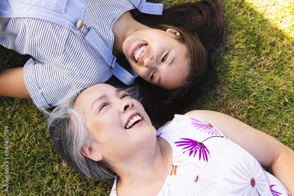 Asian grandmother and biracial granddaughter lying on grass, smiling and having fun Asian grandmother and biracial granddaughter lying on grass, smiling and having fun