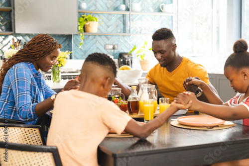 African American family saying grace around table, preparing for lunch