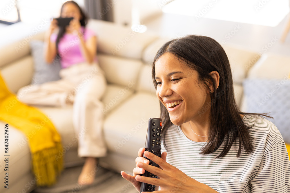 Two young biracial friends enjoying time together, one holding remote and smiling, at home Two young biracial friends enjoying time together, one holding remote and smiling, at home