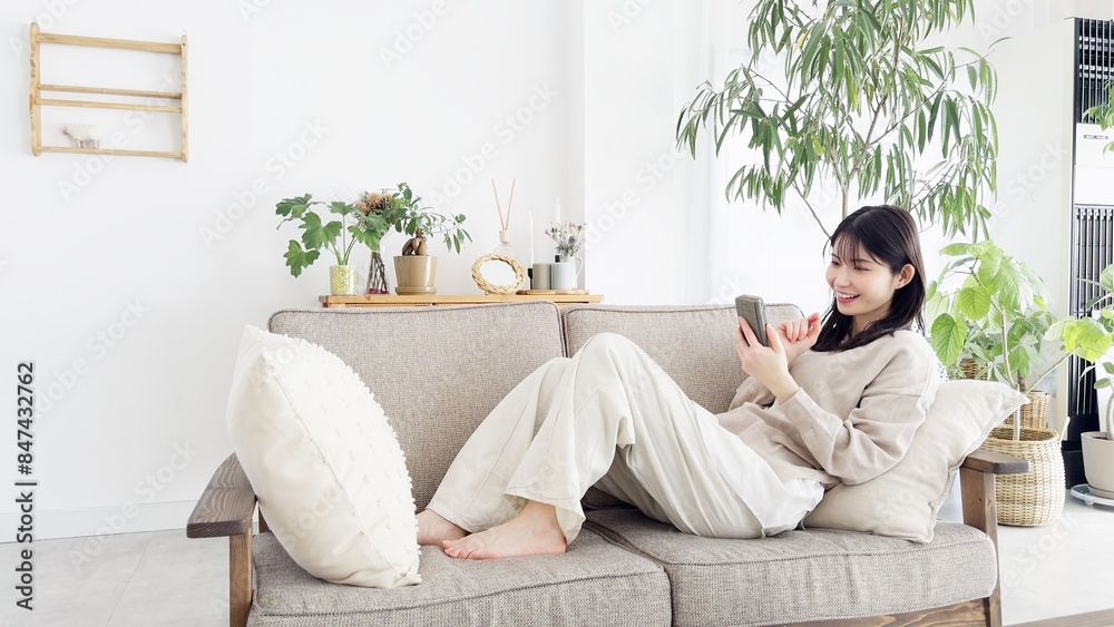 ソファでくつろぎながらスマホを見る女性 ソファでくつろぎながらスマホを見る女性