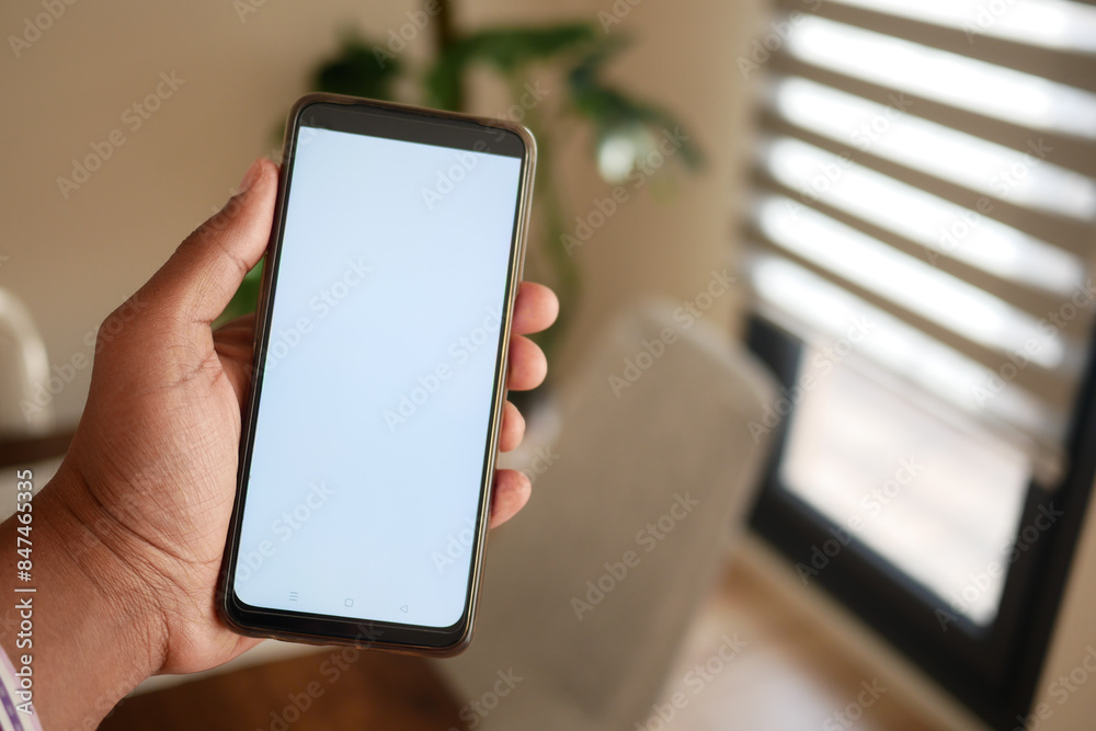 A hand holds a smartphone in a modern home interior, highlighting technology and lifestyles A hand holds a smartphone in a modern home interior, highlighting technology and lifestyles