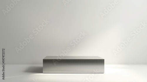 Minimalist photo of a sleek metallic rectangular object against a plain white wall with natural lighting creating soft shadows.