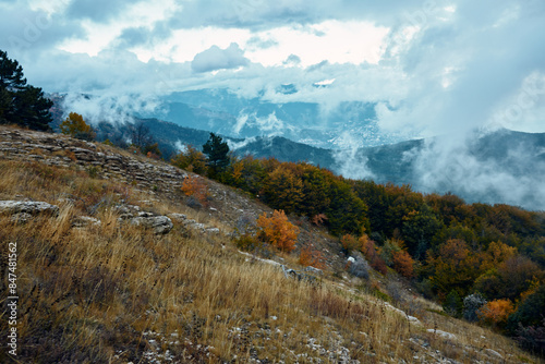 Scenic mountain landscape with dramatic clouds above trees and grass on the hillside, perfect for travel or nature themed projects photo