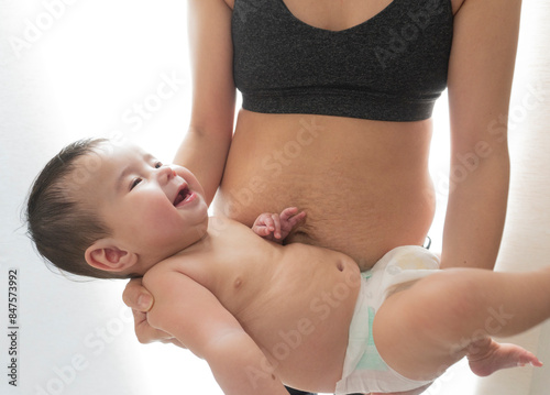 Sporty Asian woman with stretch marks after childbirth holds her baby boy. Close up view. photo