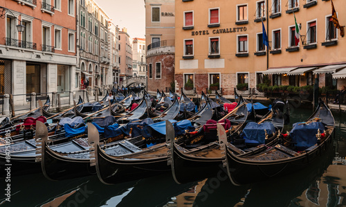 Fleet of gondolas docked in water between buildings in Venice, Italy. © Cavan