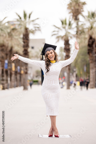 Women in white dress and graduation cap, throwing hands up in ex photo