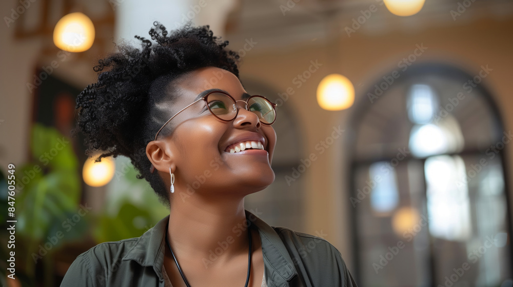 A woman with curly hair and glasses is smiling. She is wearing a green shirt and a necklace. African American woman smiling, looking up with a beautiful architectural office A woman with curly hair and glasses is smiling. She is wearing a green shirt and a necklace. African American woman smiling, looking up with a beautiful architectural office