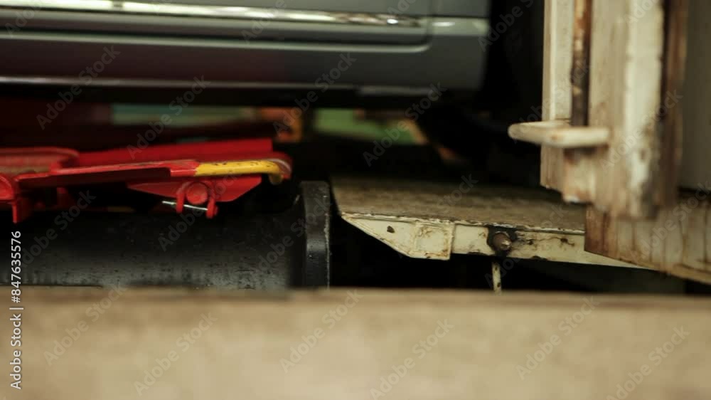 Close-up of a car on a hydraulic lift in a workshop, detailing the lift mechanism and tire Close-up of a car on a hydraulic lift in a workshop, detailing the lift mechanism and tire