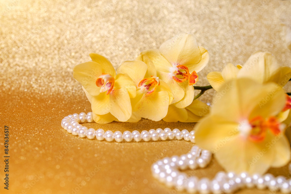 yellow Orchid and pearl necklace on a shiny gold background

