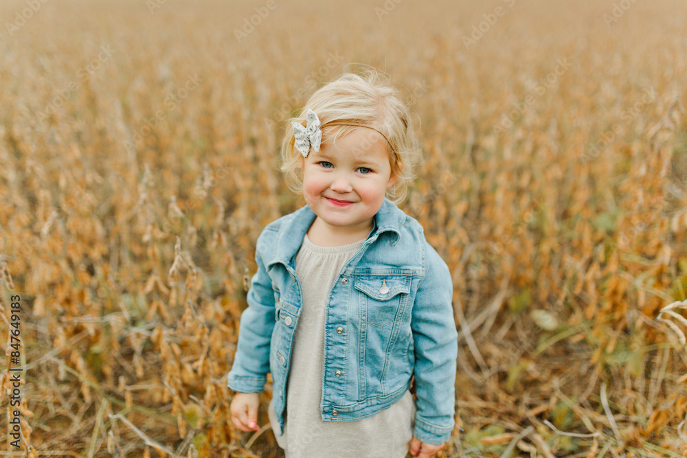 Blonde little girl smiles in a jean jacket in a field Blonde little girl smiles in a jean jacket in a field