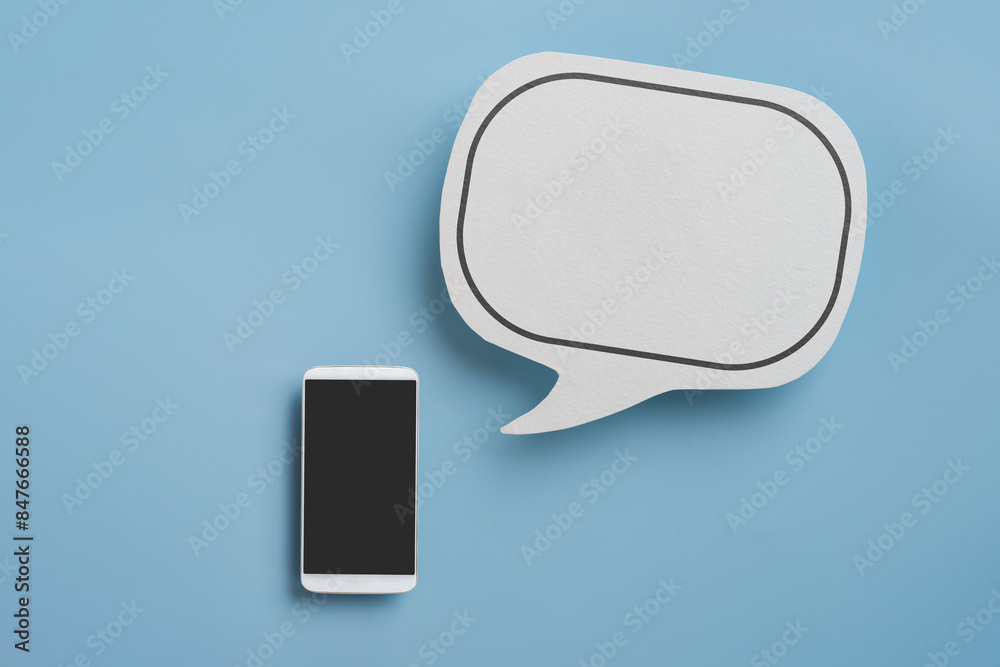 Fototapeta premium real blank white speech bubble paper cut and smartphone on blue background, top view