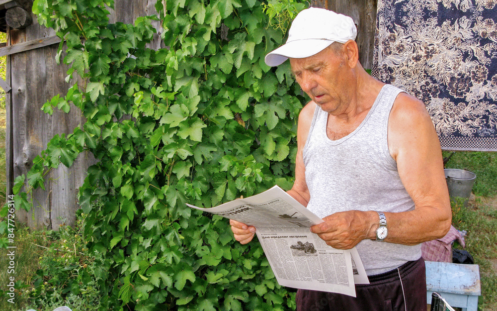 an elderly man reading a newspaper in his yard on a summer day an elderly man reading a newspaper in his yard on a summer day