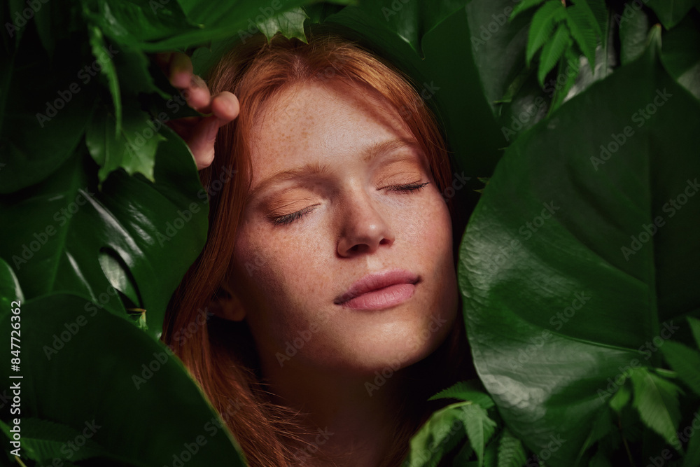 Skin care portrait of a beautiful young woman with red hair and freckles with leaves around her face. Woman who feels good. Woman who feels relaxed. Skin care portrait of a beautiful young woman with red hair and freckles with leaves around her face. Woman who feels good. Woman who feels relaxed.