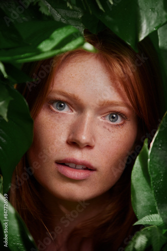 Skin care portrait of a beautiful young woman with red hair and freckles with leaves around her face. Woman smiling into the camera. 