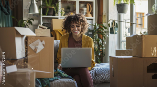 A cheerful young woman unpacks boxes in her new home, sitting on the floor surrounded by plants and basking in her newfound space and independence.