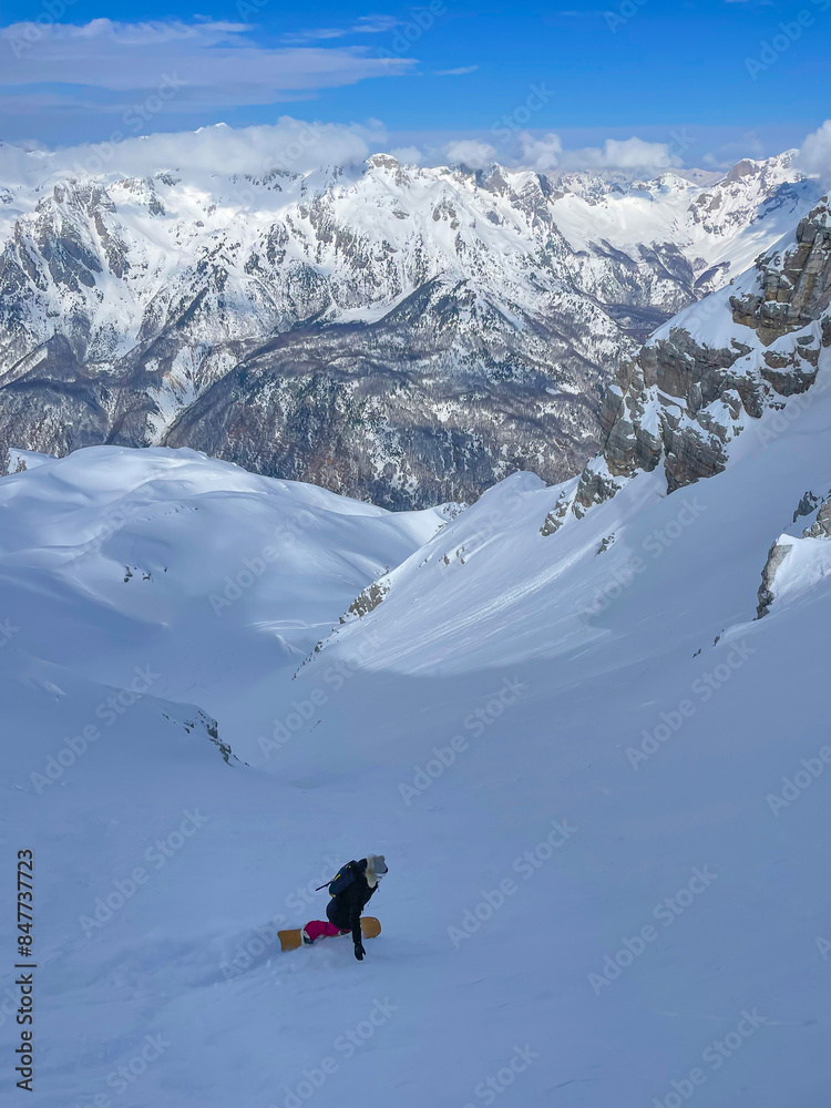 Snowy mountainside with stunning view and snowboarder descending on fresh powder Snowy mountainside with stunning view and snowboarder descending on fresh powder
