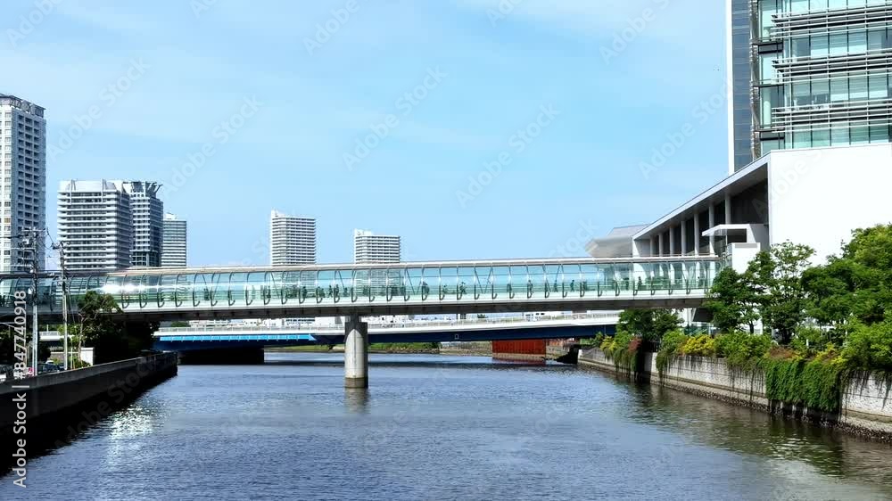 Modern cityscape with a sleek pedestrian bridge over a calm river on a sunny day Modern cityscape with a sleek pedestrian bridge over a calm river on a sunny day