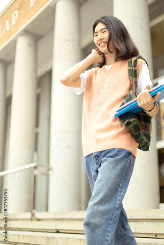 Smiling student with folders walking by university.