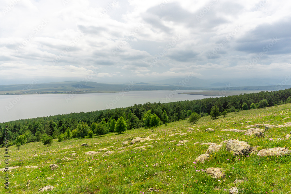 Huge stones on a grassy slope, a strip of coniferous trees, Tsalka reservoir, heavy clouds Huge stones on a grassy slope, a strip of coniferous trees, Tsalka reservoir, heavy clouds
