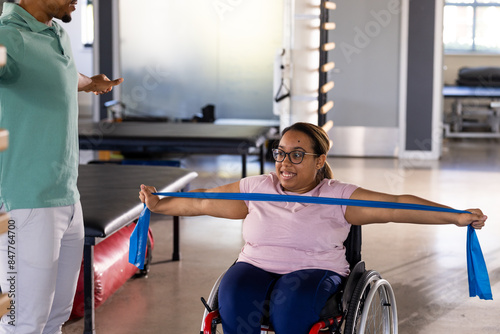 Quadriplegic biracial woman in wheelchair exercising with resistance band, copy space photo