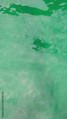 Texture of emerald green water ripples with sun glares. Vertical video 4K of nature background for shorts or stories, living wall, social media. Calm summertime vibes. Warm sunny day of summer holiday