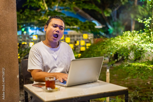 Young Asian man, digital nomad working remotely from cafe, using laptop and smartphone. young Asian men are hanging out in a cafe with a nature theme at night