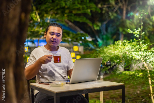Obraz na płótnie Young Asian man, digital nomad working remotely from cafe, using laptop and smartphone. young Asian men are hanging out in a cafe with a nature theme at night w salonie