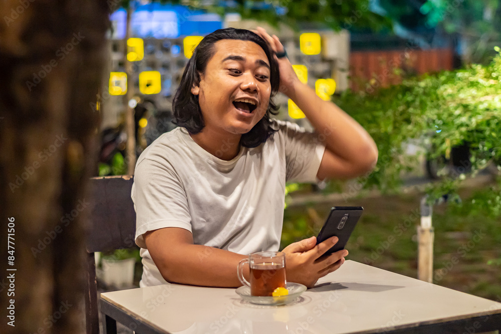Young Asian man, digital nomad working remotely from cafe, using laptop and smartphone. young Asian men are hanging out in a cafe with a nature theme at night