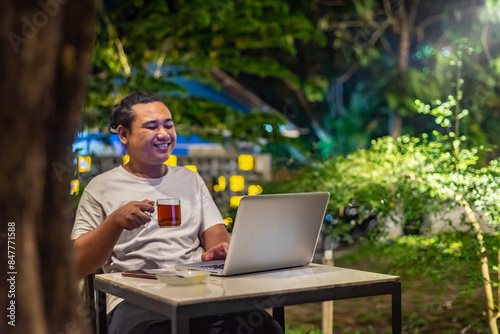 Obraz na płótnie Young Asian man, digital nomad working remotely from cafe, using laptop and smartphone. young Asian men are hanging out in a cafe with a nature theme at night w salonie