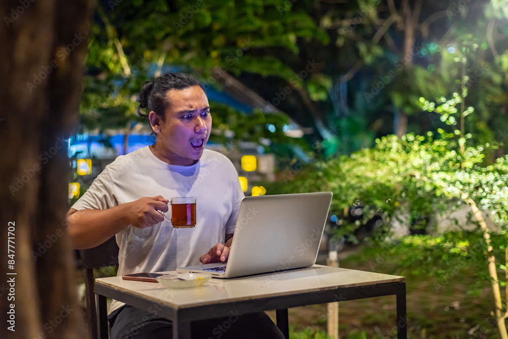Young Asian man, digital nomad working remotely from cafe, using laptop and smartphone. young Asian men are hanging out in a cafe with a nature theme at night