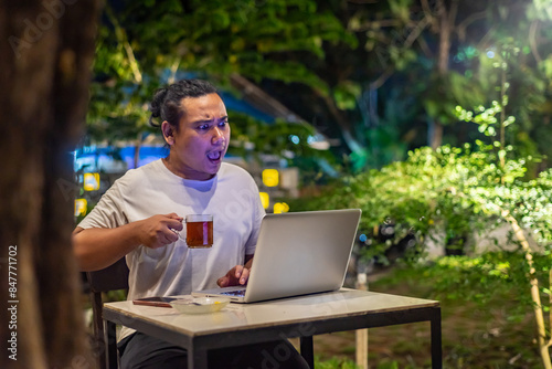 Obraz na płótnie Young Asian man, digital nomad working remotely from cafe, using laptop and smartphone. young Asian men are hanging out in a cafe with a nature theme at night w salonie
