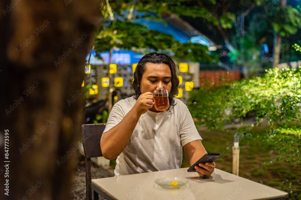 Young Asian man, digital nomad working remotely from cafe, using laptop and smartphone. young Asian men are hanging out in a cafe with a nature theme at night