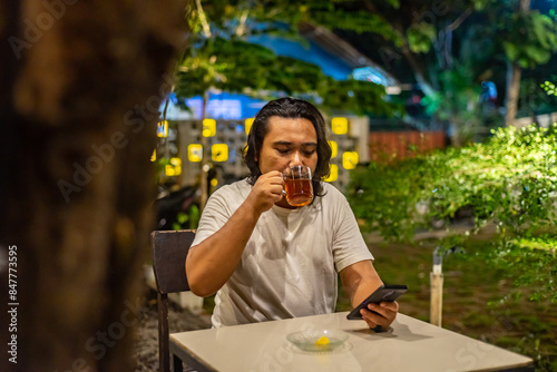 Obraz na płótnie Young Asian man, digital nomad working remotely from cafe, using laptop and smartphone. young Asian men are hanging out in a cafe with a nature theme at night w salonie