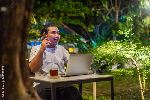 Obraz na płótnie Young Asian man, digital nomad working remotely from cafe, using laptop and smartphone. young Asian men are hanging out in a cafe with a nature theme at night w salonie