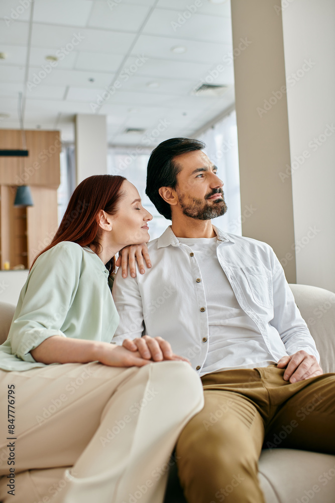 A beautiful adult couple, a redhead woman and a bearded man, sit on a couch in a modern living room, spending quality time together. A beautiful adult couple, a redhead woman and a bearded man, sit on a couch in a modern living room, spending quality time together.