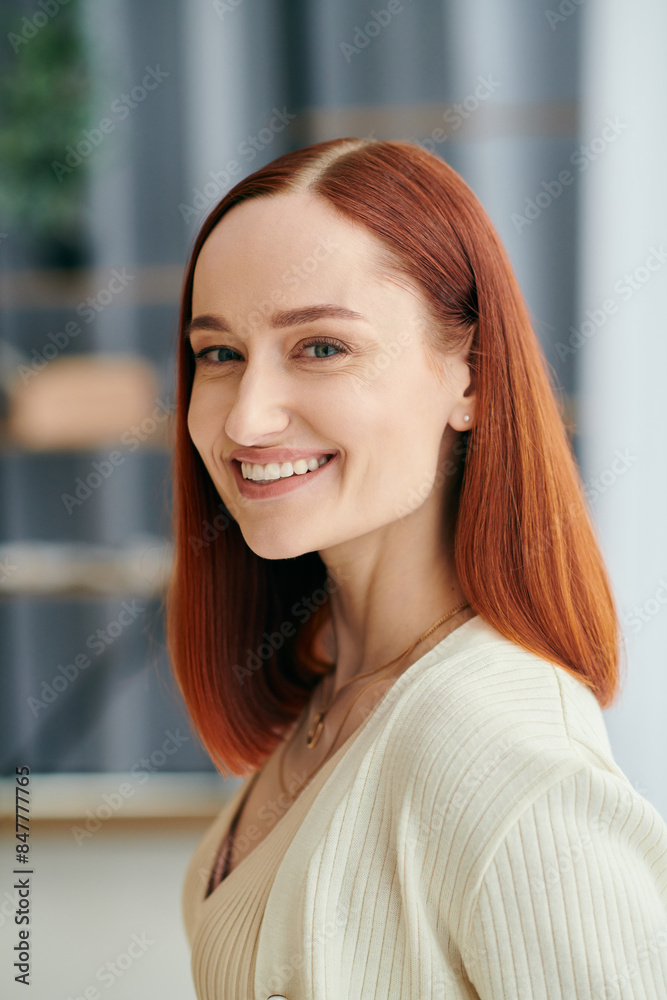 A crimson-haired woman smiling warmly at the camera, exuding happiness and comfort in a modern apartment setting. A crimson-haired woman smiling warmly at the camera, exuding happiness and comfort in a modern apartment setting.