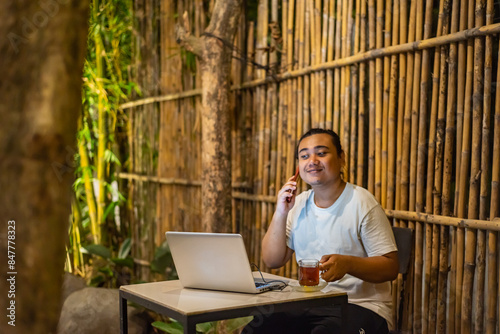 Obraz na płótnie Young Asian man, digital nomad working remotely from cafe, using laptop and smartphone. young Asian men are hanging out in a cafe with a nature theme at night w salonie