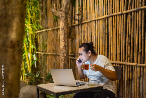 Obraz na płótnie Young Asian man, digital nomad working remotely from cafe, using laptop and smartphone. young Asian men are hanging out in a cafe with a nature theme at night w salonie