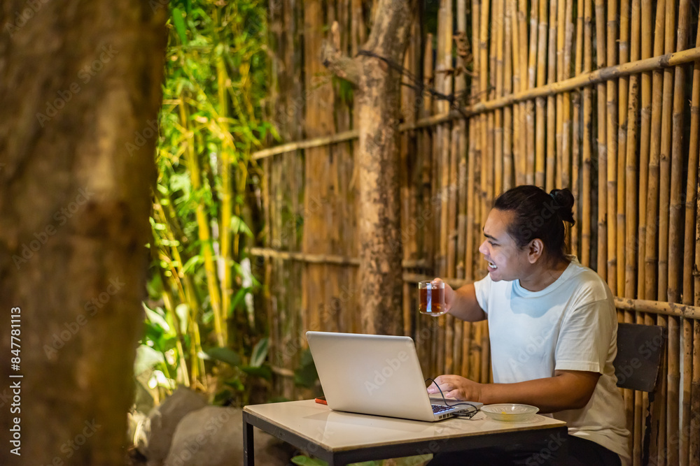 Young Asian man, digital nomad working remotely from cafe, using laptop and smartphone. young Asian men are hanging out in a cafe with a nature theme at night