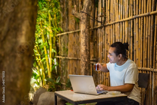 Obraz na płótnie Young Asian man, digital nomad working remotely from cafe, using laptop and smartphone. young Asian men are hanging out in a cafe with a nature theme at night w salonie