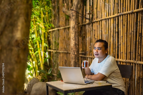 Obraz na płótnie Young Asian man, digital nomad working remotely from cafe, using laptop and smartphone. young Asian men are hanging out in a cafe with a nature theme at night w salonie