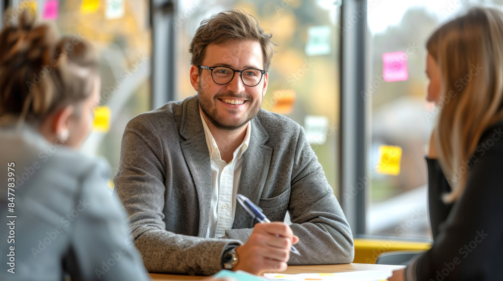 Smiling Young Businessman in a Collaborative Office Meeting, Engaging with Colleagues and Sharing Ideas