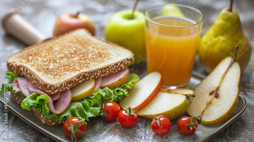 Wide-angle shot of a fresh school lunch featuring a ham and lettuce sandwich, cherry tomatoes, pear slices, and a glass of apple juice.
