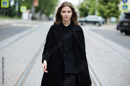 Attractive caucasian young woman in black coat walking down city street on warm autumn day. Outdoors portrait. Model in stylish clothes. Lifestyle, fashion concept. © Павел Костенко
