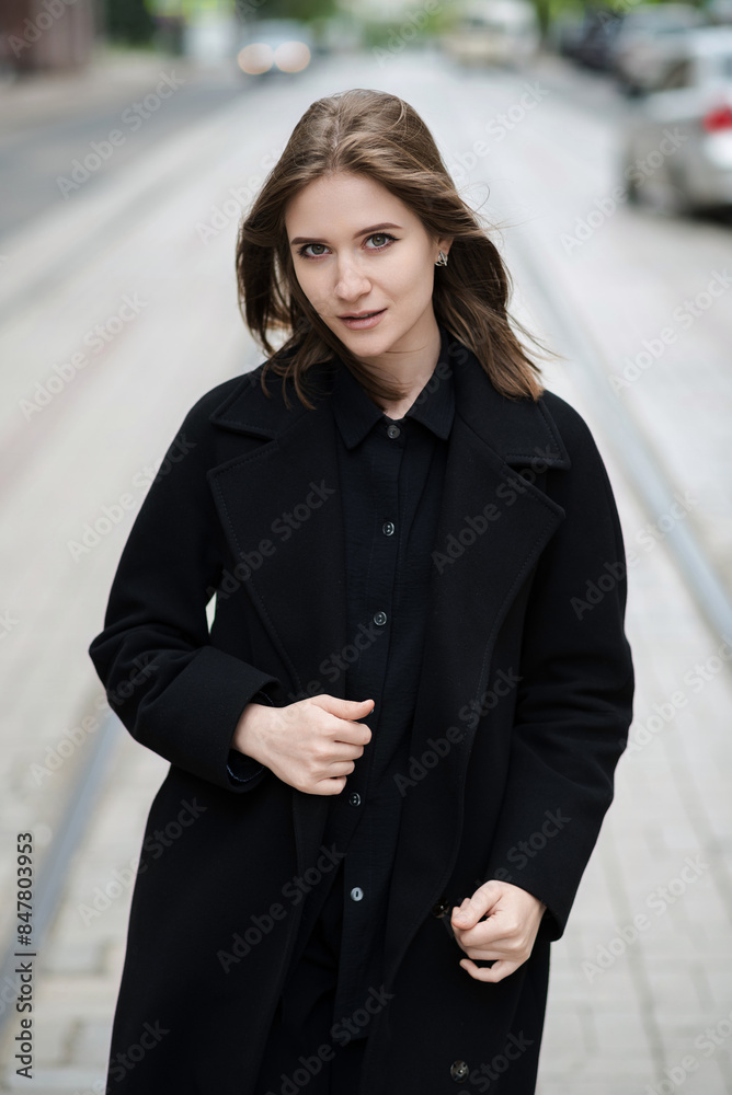 Attractive caucasian young woman in black coat walking down city street on warm autumn day. Outdoors portrait. Model in stylish clothes. Lifestyle, fashion concept. Attractive caucasian young woman in black coat walking down city street on warm autumn day. Outdoors portrait. Model in stylish clothes. Lifestyle, fashion concept.
