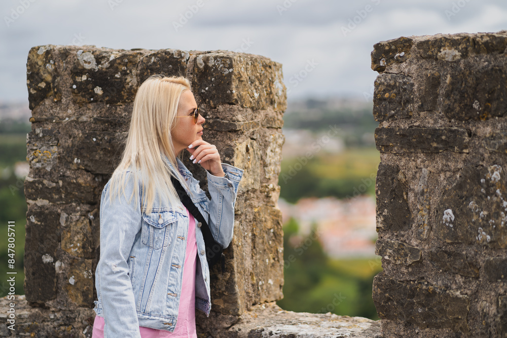 Naklejka premium A blonde tourist girl near the city wall of the Obidus fortress on a summer day.