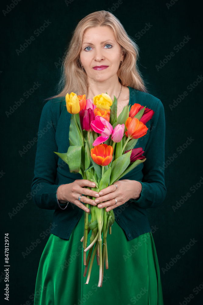 Portrait of a beautiful blonde adult woman with a bouquet of tulip flowers on a dark background. Portrait of a beautiful blonde adult woman with a bouquet of tulip flowers on a dark background.